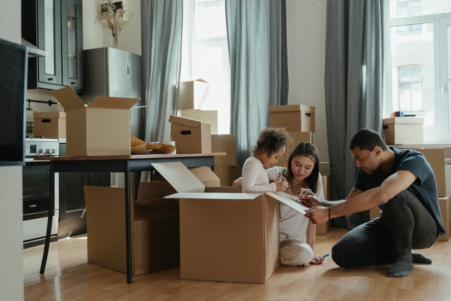 A family unpacking cardboard boxes on the floor of their new home